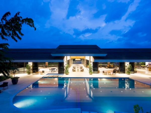A luxurious modern building with large, illuminated outdoor pool and seating areas, set against a twilight sky.