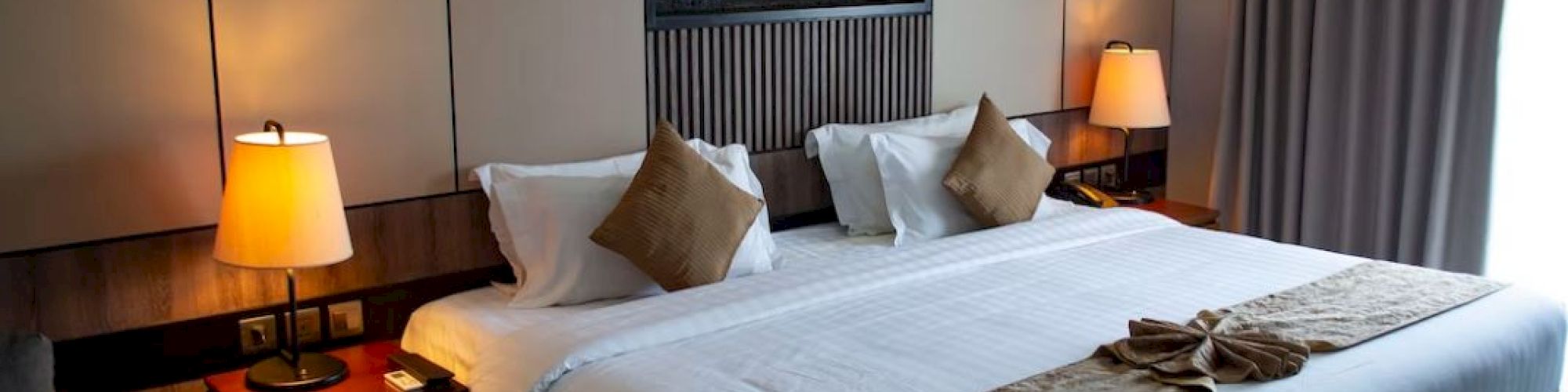 A neatly made hotel room bed with lamps, pillows, and decorative elements, offering a cozy and inviting atmosphere.
