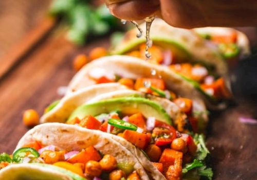 A hand squeezes lime juice over tacos filled with chickpeas, avocado, and veggies, garnished with cilantro, on a wooden board.