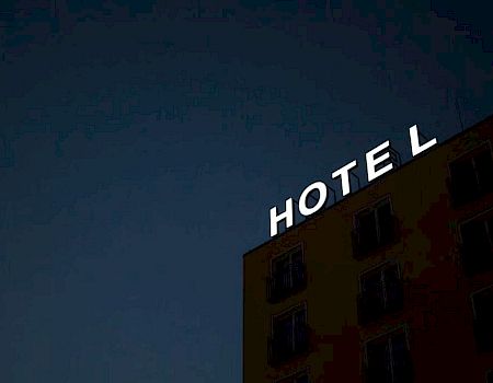 A building with the illuminated word "HOTEL" on the roof, set against a dark evening sky.