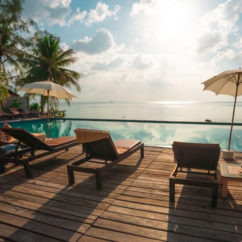 Poolside scene with lounge chairs, umbrellas, and a view of the ocean under a cloudy sky, evoking a serene beach resort vibe.