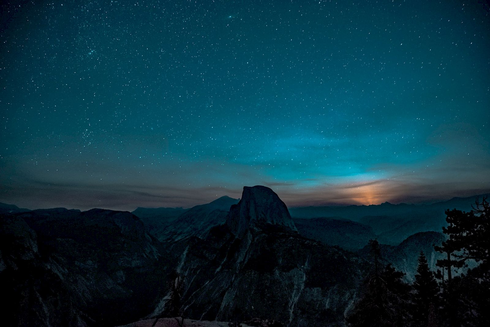 A starry night sky over a mountainous landscape, with a glowing horizon and silhouetted peaks below the sky.