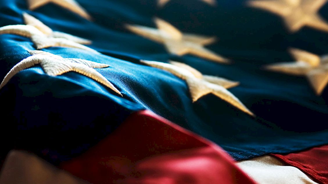 An American flag with visible stars and stripes is shown, focusing on the blue field and white stars.