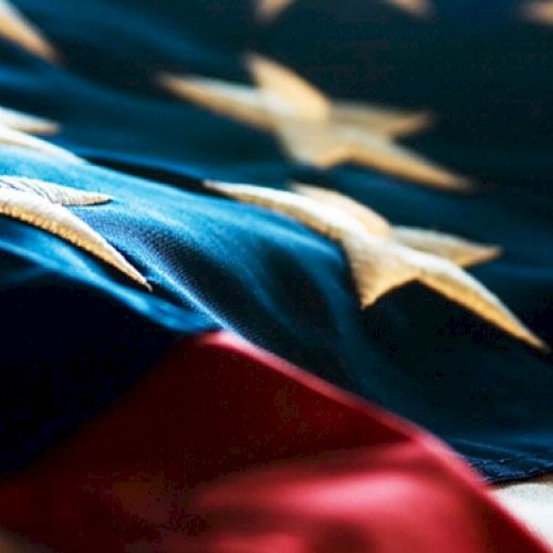 This image shows a close-up of an American flag, displaying its stars and red and blue stripes in a slightly out-of-focus perspective.