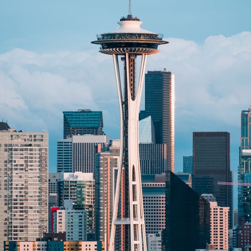 The image shows a city skyline with a prominent observation tower featuring a unique design, surrounded by modern skyscrapers.