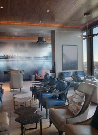 A modern lounge with plush seating, large windows with a view of a waterfront and Ferris wheel, and ambient lighting on the ceiling.