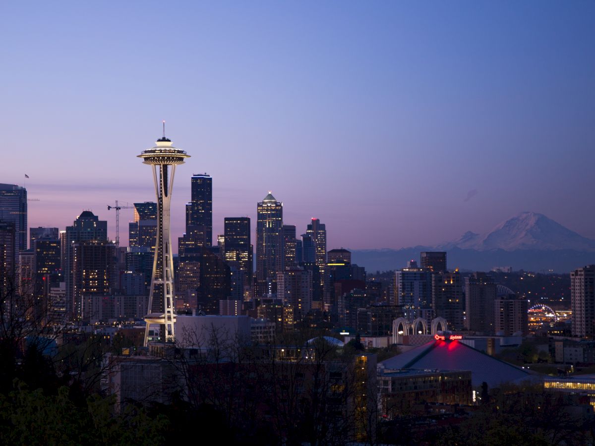 The image shows the Seattle skyline at dusk, featuring the Space Needle and Mount Rainier in the background, creating a scenic urban view.